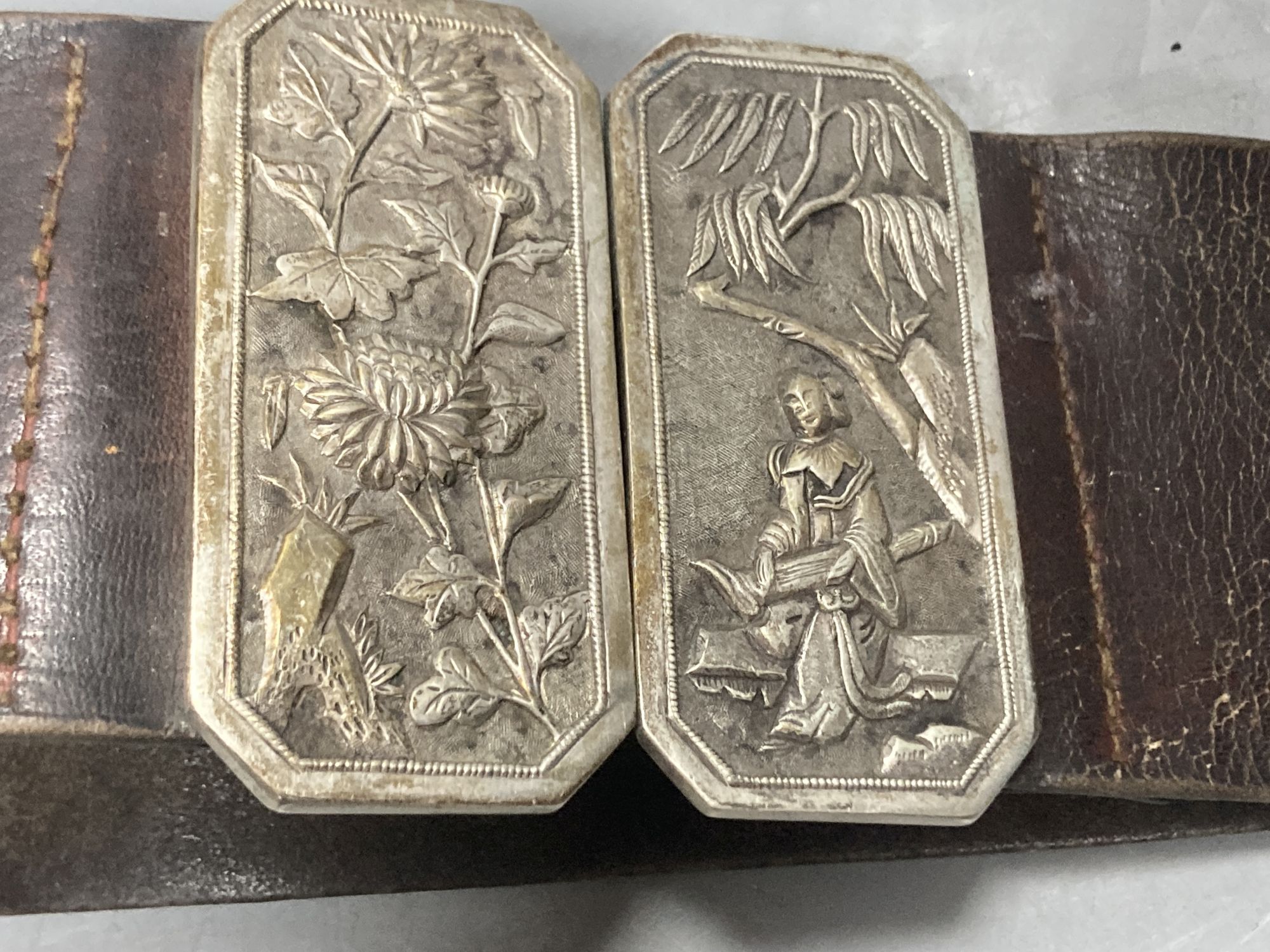 A Chinese white metal cigarette case by Luen Hing, 75mm and four pairs of Chinese white metal belt buckles, three mounted on leather